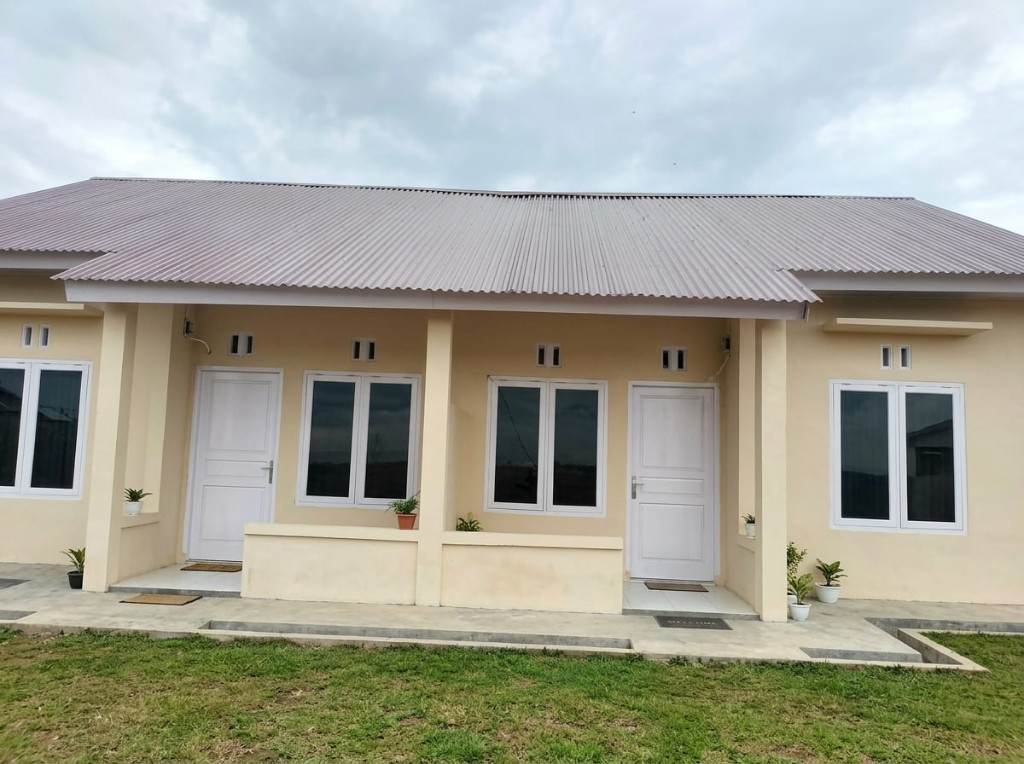 Rumah krem beratap seng dengan pintu putih dan teras