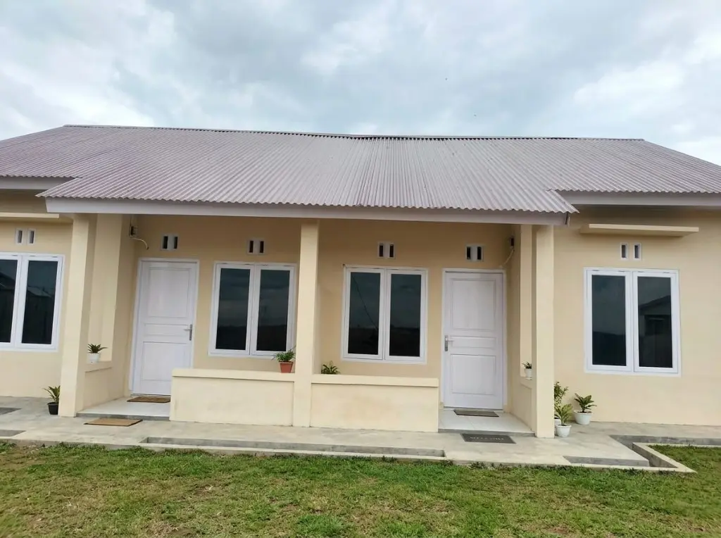 Rumah krem beratap seng dengan pintu putih, jendela, dan teras